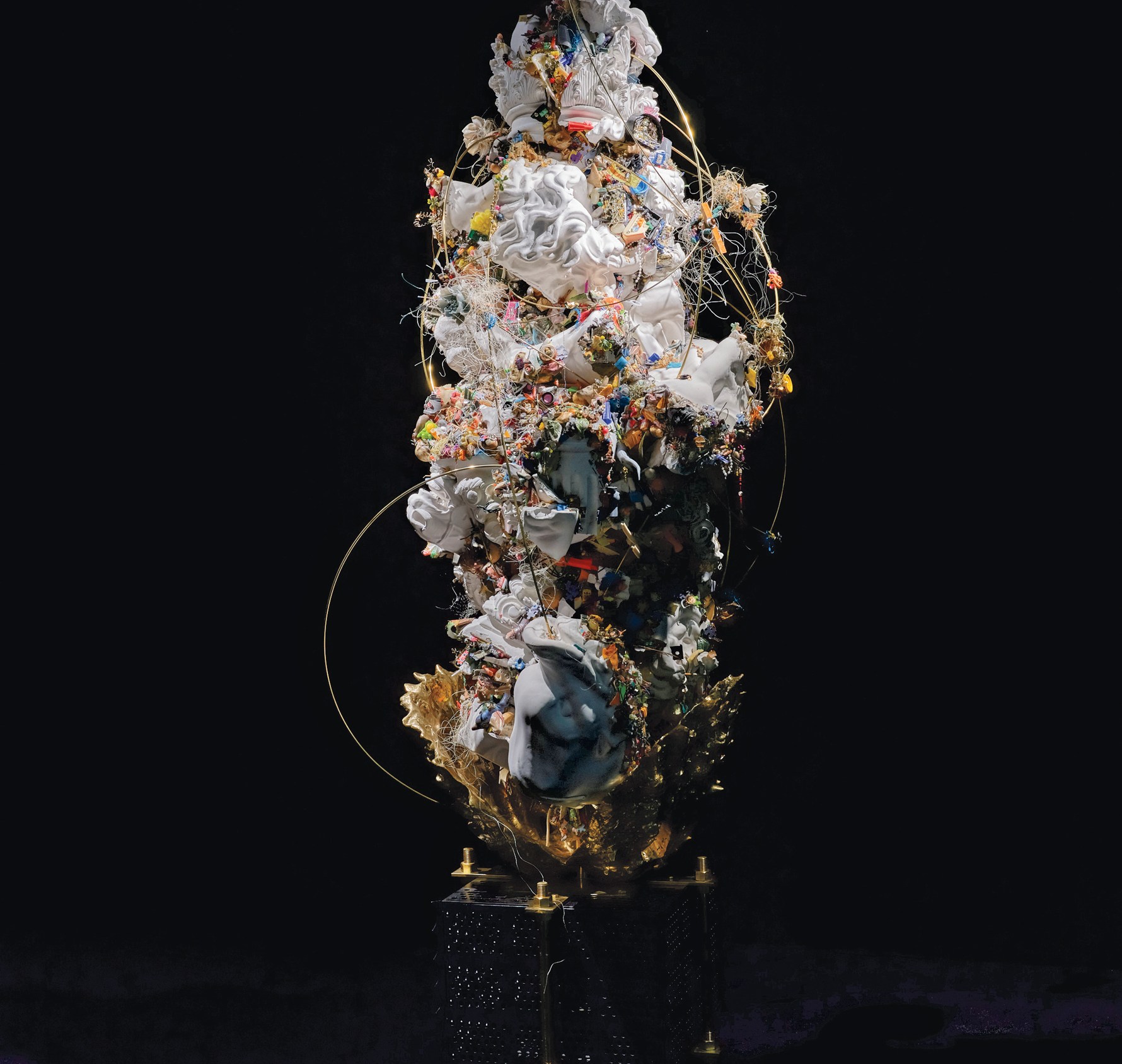 A vertical mixed-media sculpture with white porcelain shards, colorful debris, gold accents, wire loops, and intricate textures on a black pedestal.