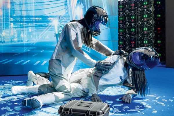 Two figures in helmets and futuristic white suits interact on a blue surface with scattered glass-like shards, a case nearby, and a digital urban backdrop.