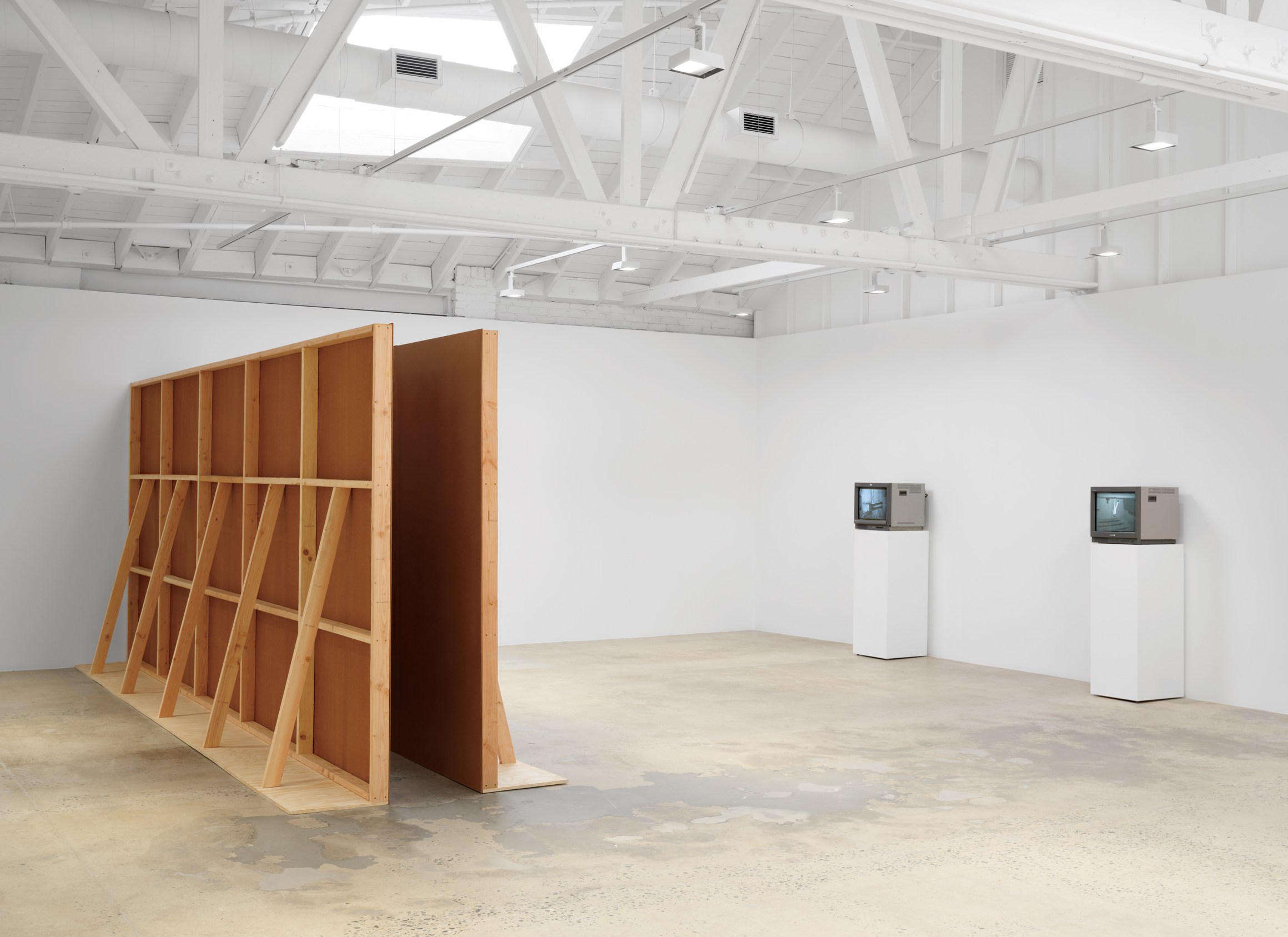 A spacious white room with exposed beams, two vintage TVs on pedestals, and a large wood-framed partition with a reddish panel in the center.