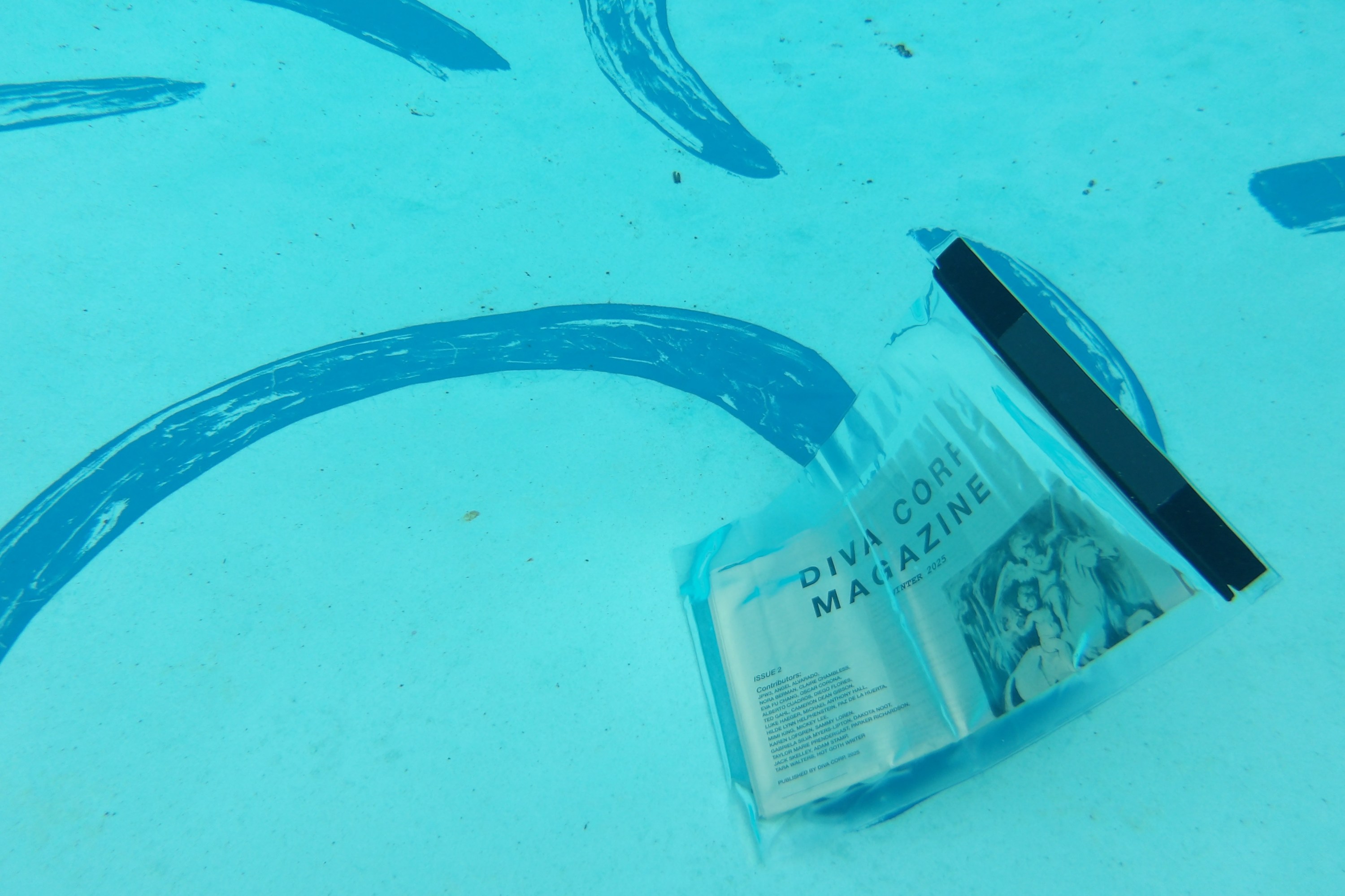 The image shows a transparent plastic bag containing a publication labeled "Diva Corp Magazine" submerged in water. The blue water has curved, painted lines on the surface, and there are small debris particles visible.