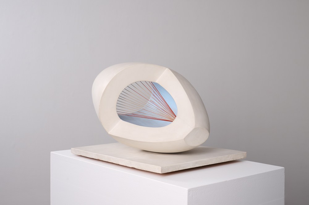 A modern abstract sculpture with a smooth, off-white oval shape featuring a hollow center. Inside, red strings are stretched in a geometric pattern against a light blue background. The sculpture is placed on a square white base.