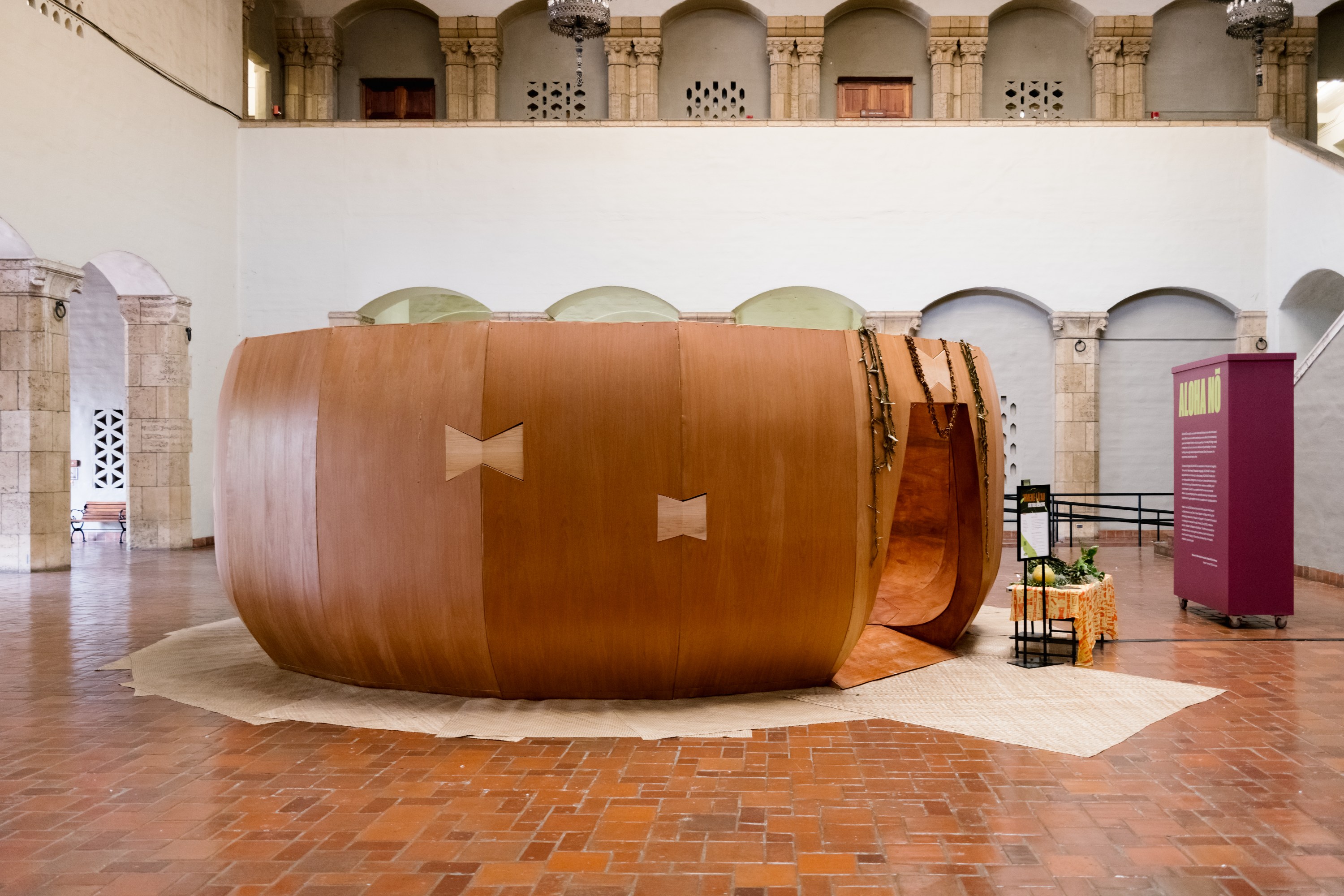 A large-scale sculptural installation in the shape of a calabash placed in the center of a museum atrium. A door-size opening is carved into its right side.
