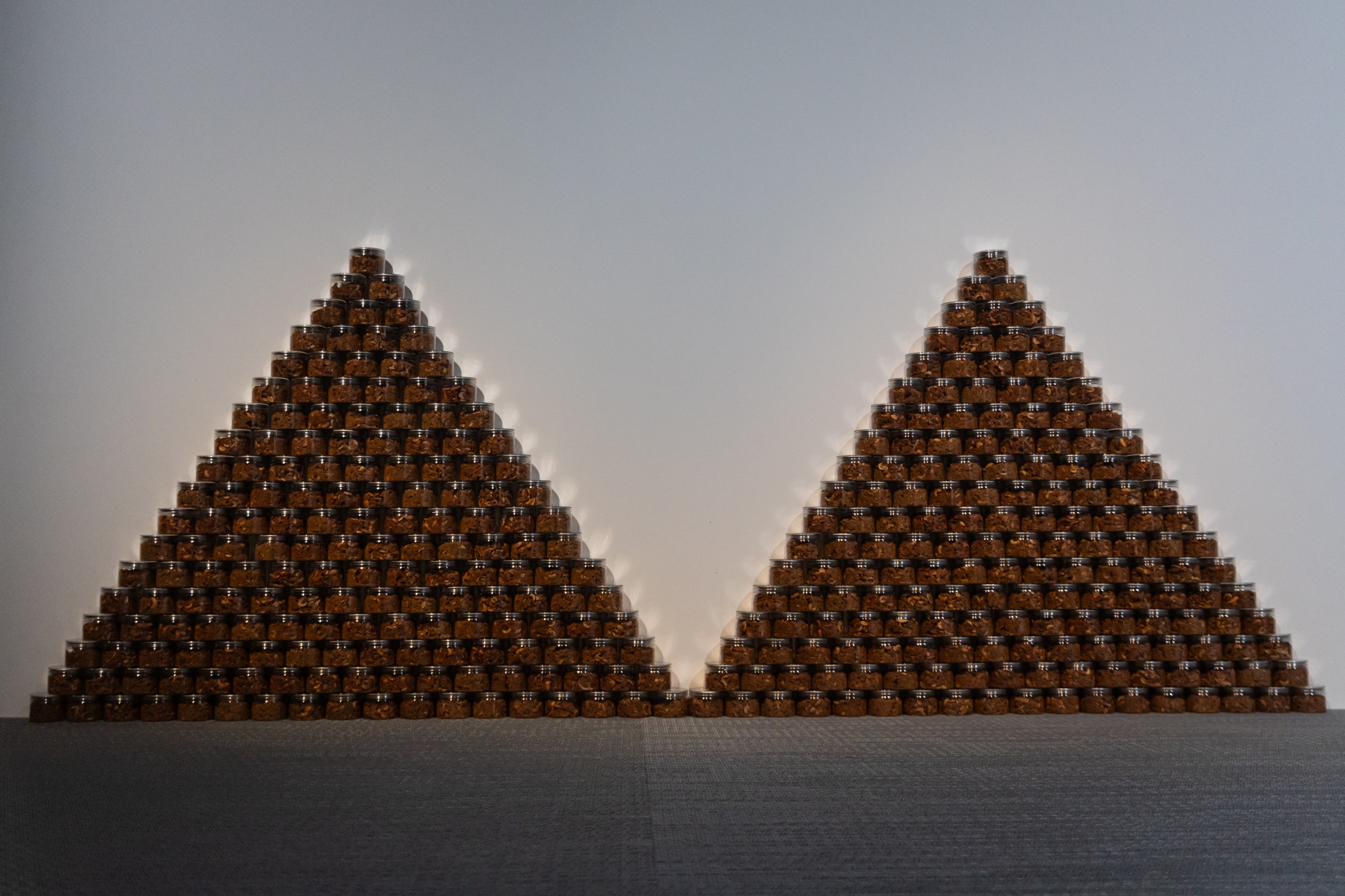 Installation view of two side-by-side pyramids made of jarred chile paste.