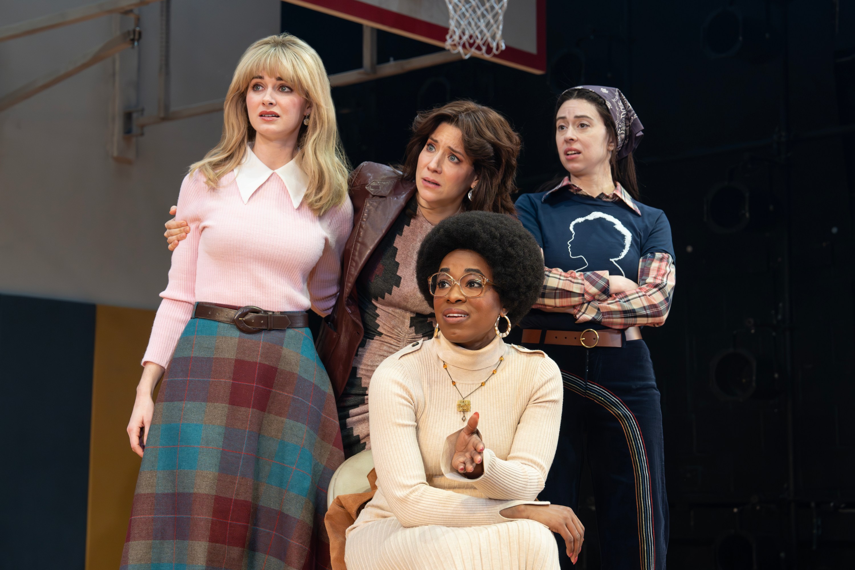 Four women on stage peering in the same direction.