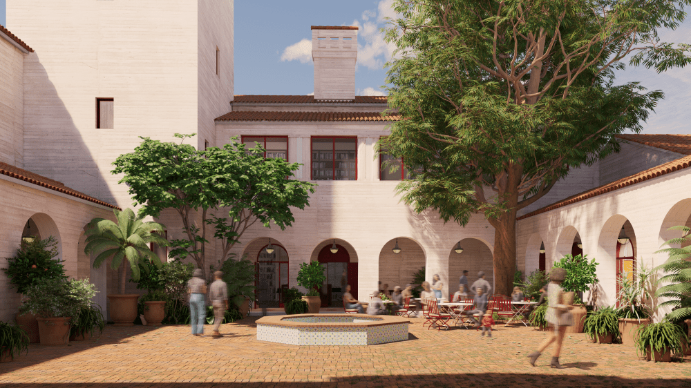 A sunny courtyard surrounded by light-colored buildings with red-tiled roofs and arched openings. The space is decorated with potted plants and trees, including a large central tree and a tiled fountain. People are walking and sitting at red tables, enjoying the calm atmosphere.